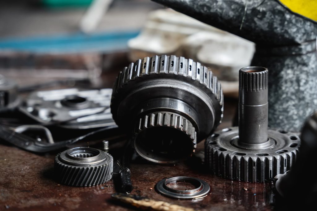 Close-up of various mechanical car parts, including metal gears and bearings, scattered on a workbench in a workshop setting.